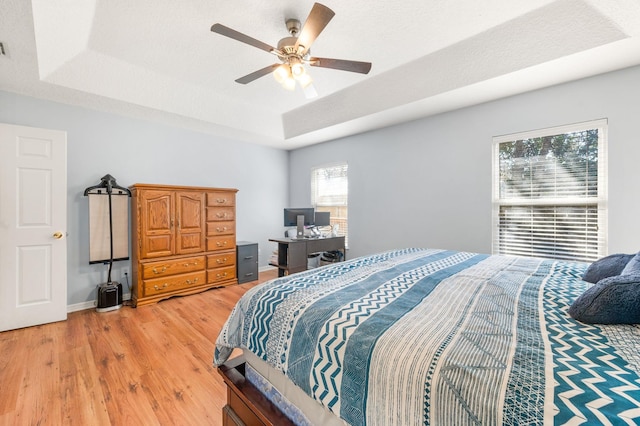 bedroom featuring a textured ceiling, wood-type flooring, a raised ceiling, and ceiling fan