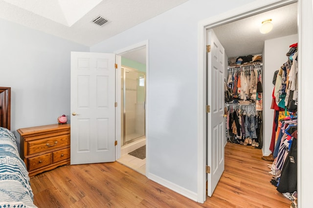 bedroom with light wood-type flooring, a walk in closet, a textured ceiling, ensuite bath, and a closet