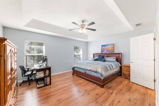 bedroom with multiple windows, a tray ceiling, light hardwood / wood-style flooring, and a textured ceiling