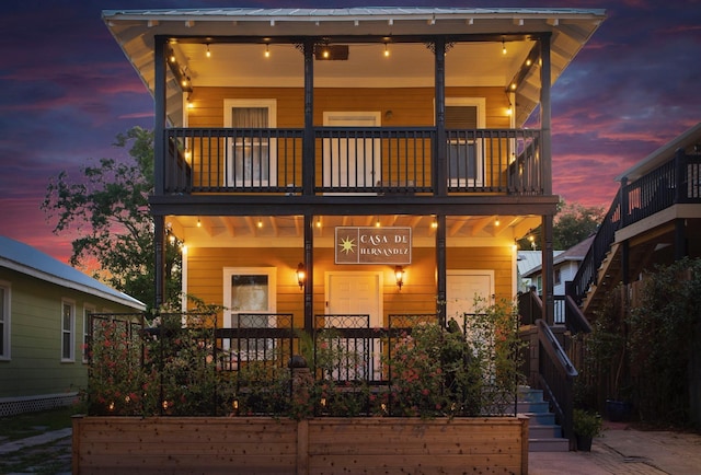 back house at dusk featuring a balcony and a porch