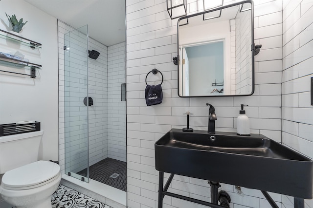 bathroom with tile patterned flooring, toilet, a shower with shower door, and tile walls