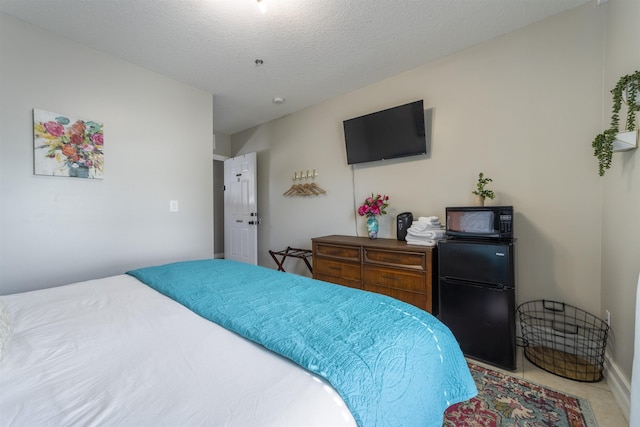 bedroom featuring tile patterned floors, black refrigerator, and a textured ceiling