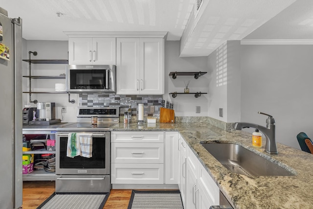 210 16th Street Unit J, Saint Augustine Beach, FL 32080 - kitchen featuring stainless steel appliances, light wood-style floors, white cabinets, crown molding, and light stone countertops