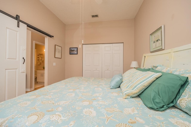 bedroom with ensuite bathroom, a barn door, a textured ceiling, and a closet