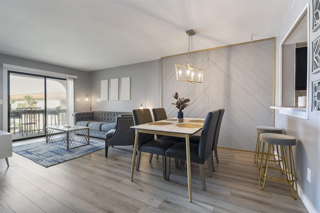 dining room with light hardwood / wood-style floors, wooden walls, and a chandelier