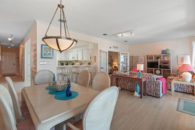 dining room with ornamental molding, light hardwood / wood-style floors, a textured ceiling, and track lighting