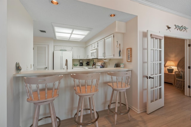 kitchen with a breakfast bar area, kitchen peninsula, white appliances, light hardwood / wood-style floors, and white cabinets