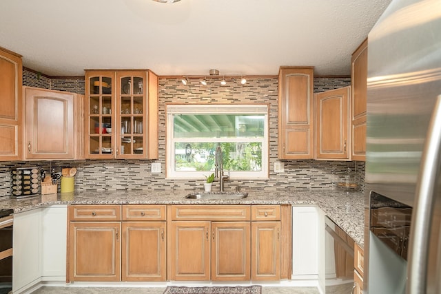 kitchen with sink, light stone counters, tasteful backsplash, range, and stainless steel fridge