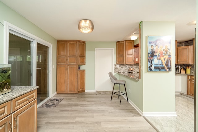 kitchen with backsplash, light stone countertops, and light wood-type flooring