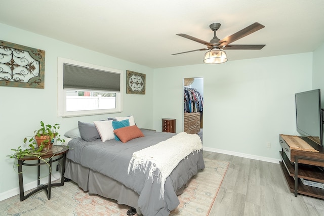 bedroom featuring ceiling fan, a spacious closet, a closet, and light hardwood / wood-style flooring