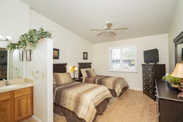 bedroom featuring lofted ceiling, sink, light hardwood / wood-style floors, and a textured ceiling