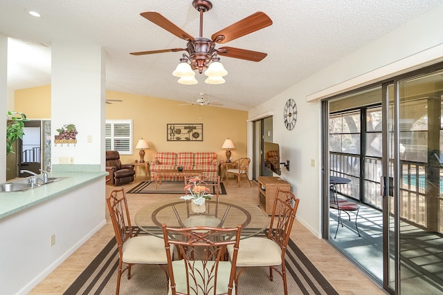 dining room with light hardwood / wood-style flooring, sink, vaulted ceiling, and a textured ceiling