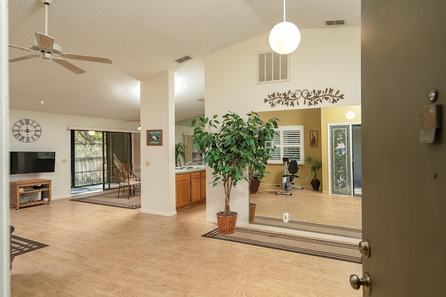 foyer entrance with ceiling fan, a textured ceiling, high vaulted ceiling, and light hardwood / wood-style flooring