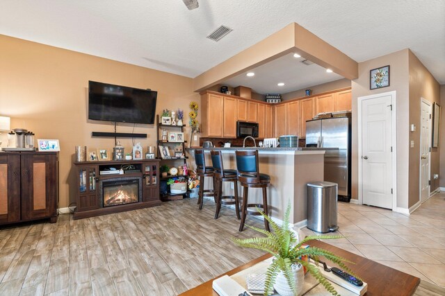 kitchen with stainless steel refrigerator with ice dispenser, light hardwood / wood-style floors, a textured ceiling, a kitchen bar, and kitchen peninsula