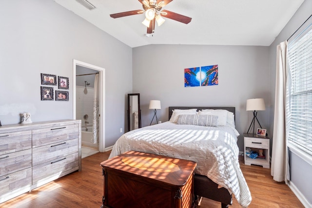 bedroom featuring lofted ceiling, ensuite bathroom, multiple windows, and light wood-type flooring