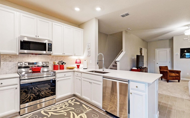 kitchen featuring a peninsula, a sink, decorative backsplash, light countertops, and appliances with stainless steel finishes