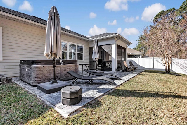 back of property featuring a sunroom, a hot tub, a patio area, and a lawn