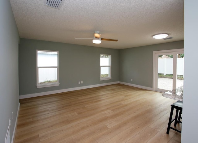 unfurnished room featuring a textured ceiling, ceiling fan, light hardwood / wood-style flooring, and plenty of natural light