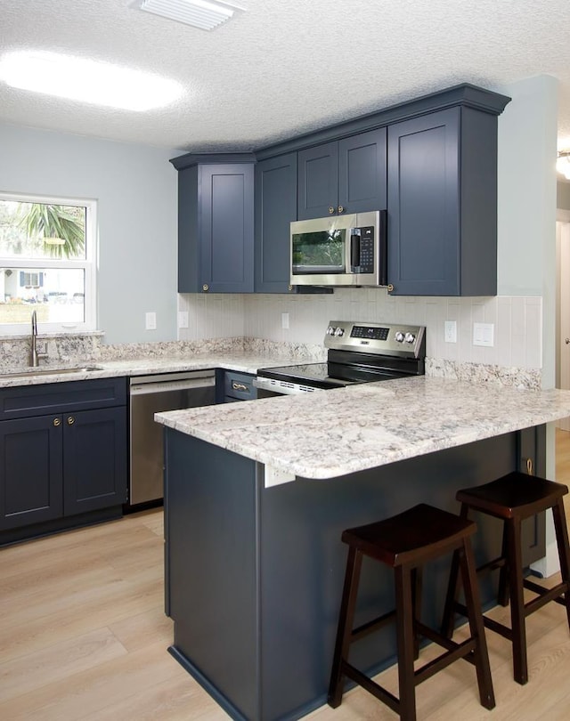 kitchen featuring a breakfast bar, stainless steel appliances, blue cabinets, sink, and light hardwood / wood-style floors