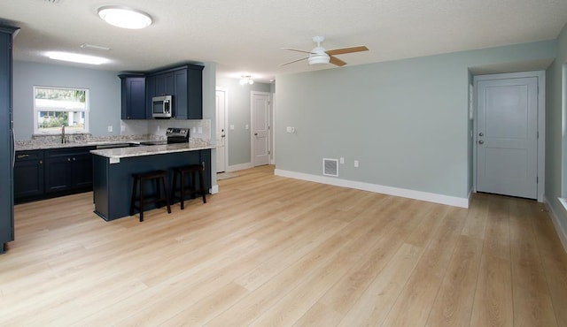 kitchen with a kitchen bar, sink, stainless steel appliances, and light hardwood / wood-style floors