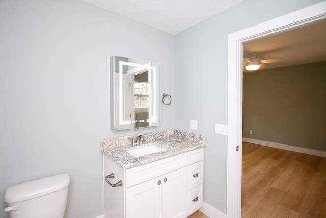 bathroom with hardwood / wood-style floors, vanity, ceiling fan, toilet, and a textured ceiling