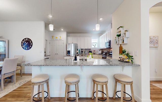 59 Oakleaf Way, Palm Coast, FL 32137 - kitchen with a peninsula, appliances with stainless steel finishes, white cabinetry, light stone countertops, and light wood-style floors