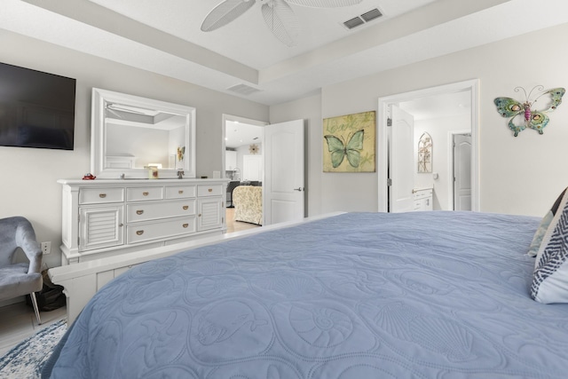 bedroom with a tray ceiling, ensuite bath, and ceiling fan