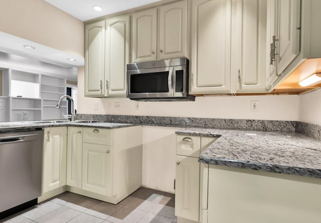 kitchen featuring sink, dark stone counters, cream cabinetry, light tile patterned floors, and appliances with stainless steel finishes