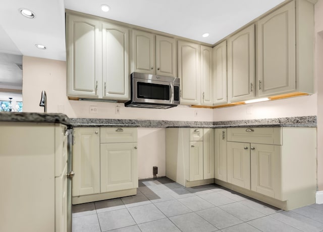 kitchen with cream cabinets, light tile patterned floors, and dark stone countertops