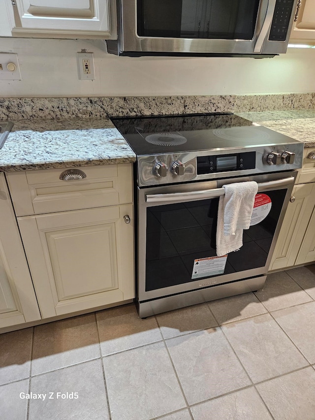 kitchen featuring light stone countertops, light tile patterned floors, stainless steel appliances, and cream cabinetry