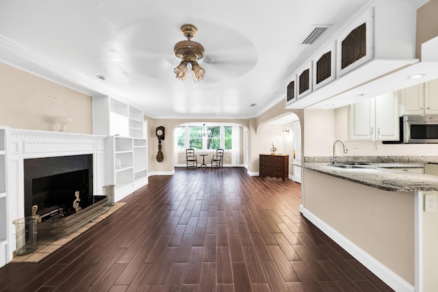 unfurnished living room with dark wood-type flooring, sink, ceiling fan, built in features, and ornamental molding