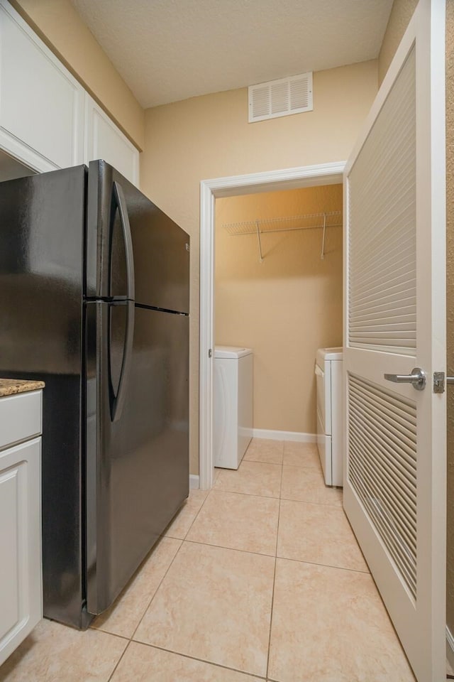 kitchen with white cabinetry, washer and clothes dryer, light tile patterned flooring, and black fridge