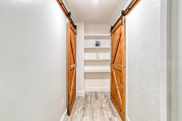 hall featuring a barn door, light hardwood / wood-style flooring, and ornamental molding