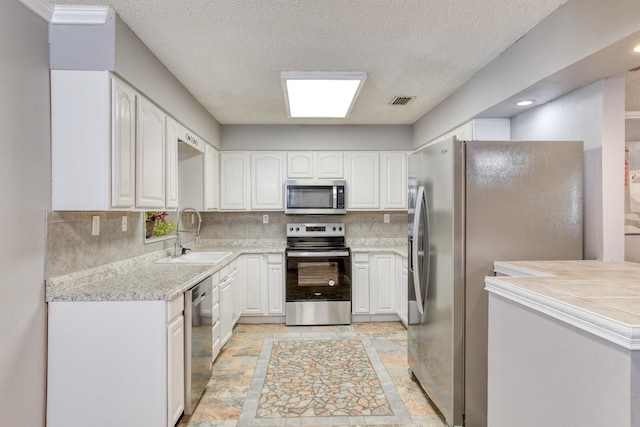 kitchen featuring white cabinetry, sink, tasteful backsplash, a textured ceiling, and appliances with stainless steel finishes