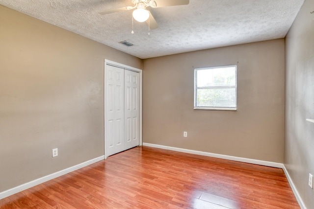 unfurnished bedroom with a closet, a textured ceiling, hardwood / wood-style flooring, and ceiling fan