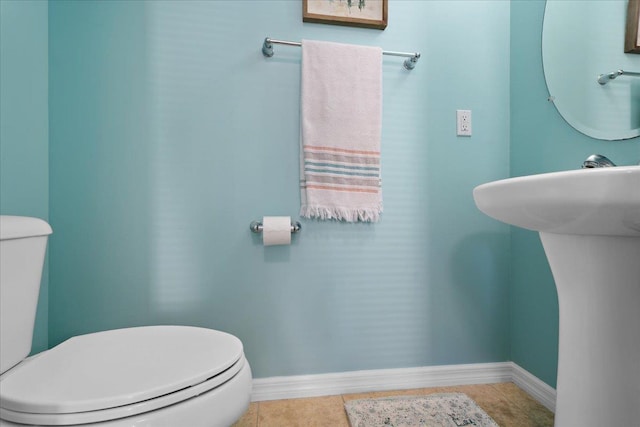 half bathroom with a sink, baseboards, toilet, and tile patterned flooring