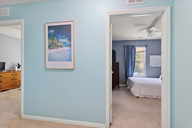 hall featuring visible vents, a textured ceiling, baseboards, and carpet floors