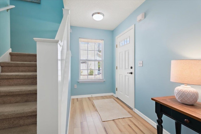 foyer entrance with baseboards, stairway, a textured ceiling, and light wood-style floors