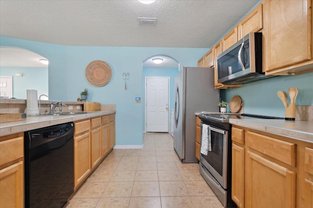 kitchen with light countertops, light tile patterned floors, arched walkways, stainless steel appliances, and a sink