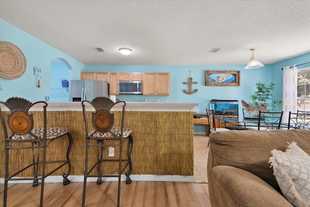 kitchen featuring visible vents, light wood-style flooring, stainless steel appliances, a breakfast bar area, and light countertops