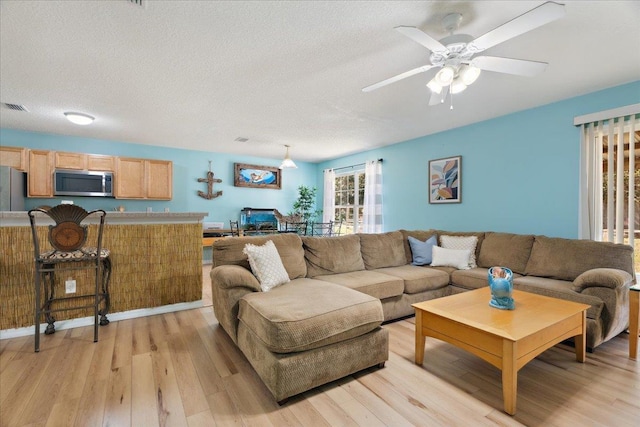 living area with visible vents, a textured ceiling, a ceiling fan, and light wood finished floors