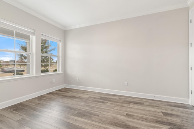 empty room featuring light wood-type flooring, baseboards, and ornamental molding