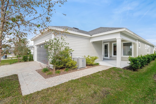 view of side of home with a garage, cooling unit, covered porch, and a lawn