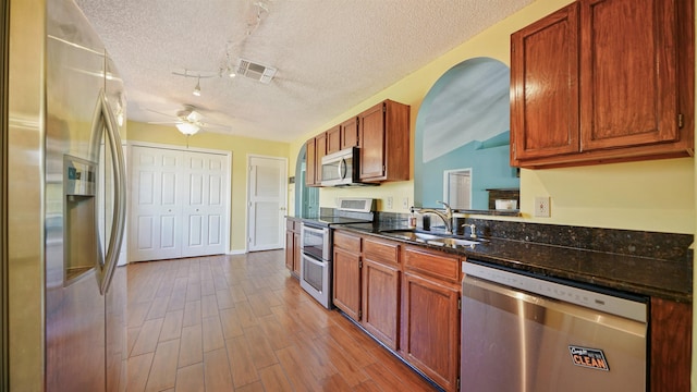 kitchen with a textured ceiling, a ceiling fan, appliances with stainless steel finishes, wood finished floors, and a sink
