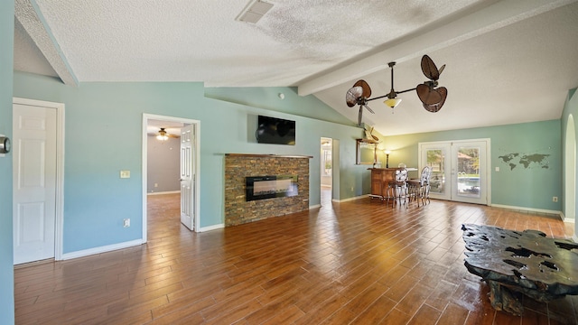 living area with baseboards, lofted ceiling with beams, a stone fireplace, a textured ceiling, and wood finished floors