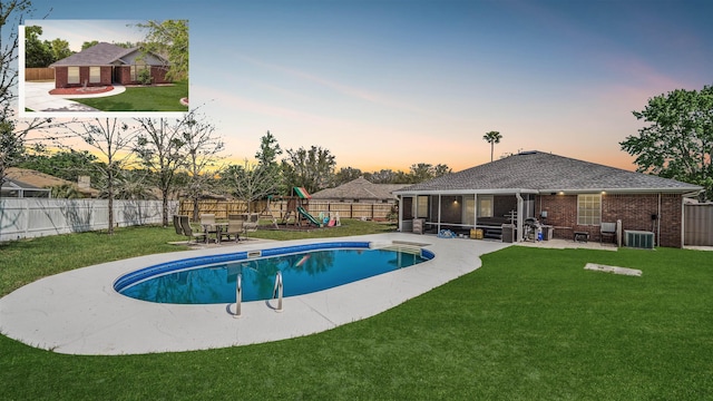 pool at dusk with a fenced in pool, a lawn, a fenced backyard, a sunroom, and a playground
