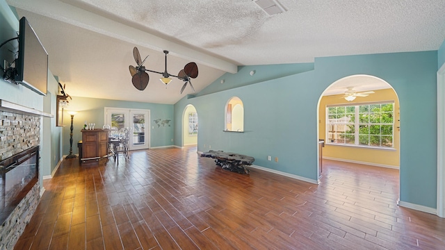 living area with arched walkways, lofted ceiling with beams, ceiling fan, a fireplace, and wood finished floors