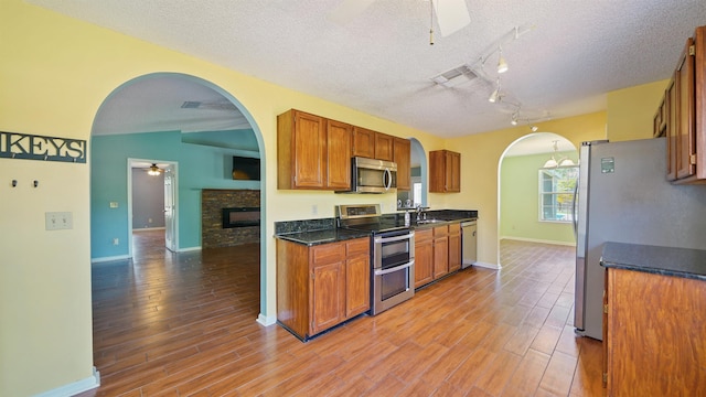 kitchen featuring arched walkways, light wood-type flooring, a ceiling fan, and appliances with stainless steel finishes
