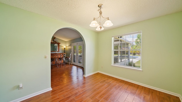 unfurnished dining area with baseboards, arched walkways, a notable chandelier, and wood finished floors