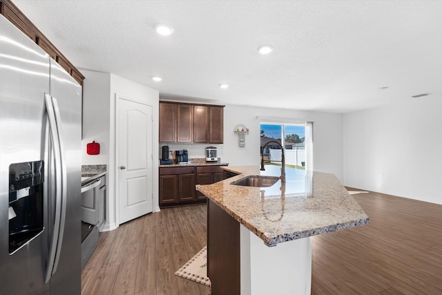 kitchen with light stone countertops, appliances with stainless steel finishes, sink, and a center island with sink